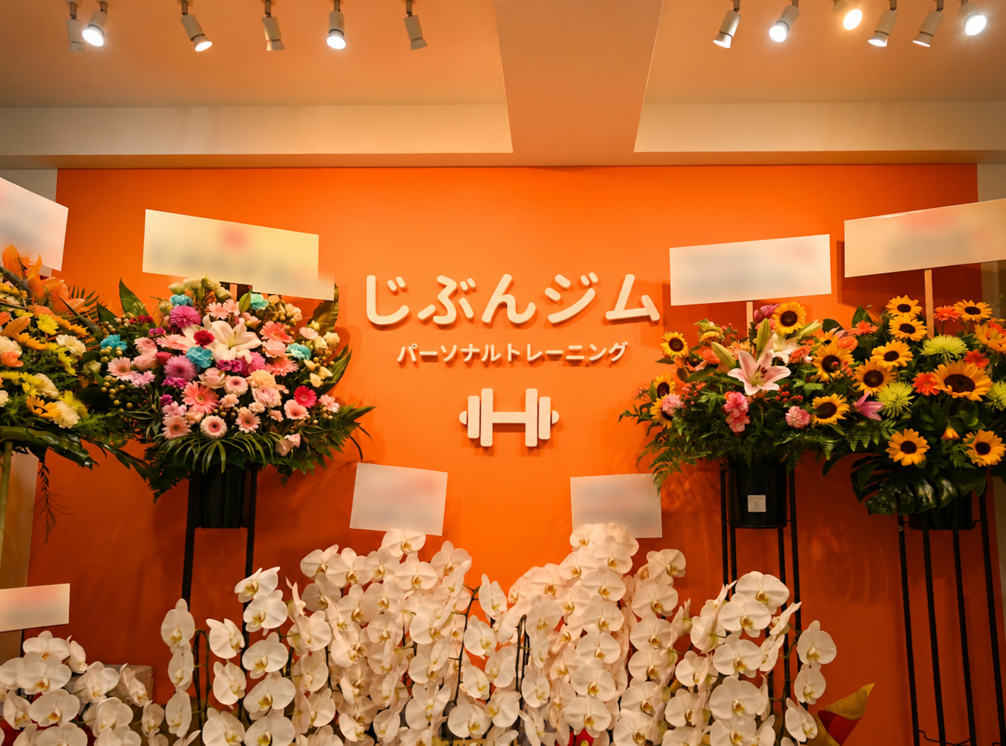じぶんジム亀有店のロゴ壁と祝い花。札の文字はぼかし処理済み